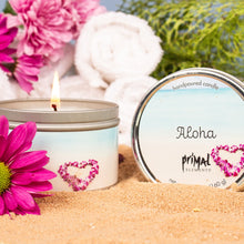 Load image into Gallery viewer, Candle with 'Aloha' label surrounded by pink flowers and towels on sand