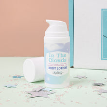 Load image into Gallery viewer, A pump bottle of body lotion labeled 'In The Clouds' positioned on a surface with decorative stars, against a pink and blue background.