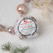 Load image into Gallery viewer, A packaged bath bomb with pomegranate and spice botanical print design, labeled 'Pomegranate Bath Bomb', placed on a decorative setting with pearls and greenery.