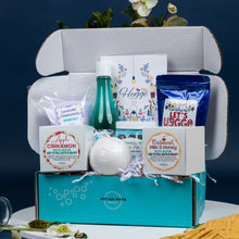 Load image into Gallery viewer, Gift box with various items including a bottle, bath bomb, and packages on a dark background