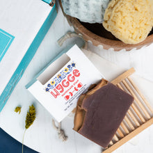 Load image into Gallery viewer, Yogee soap bar with branding on a white surface with a basket of bath bombs and a book.