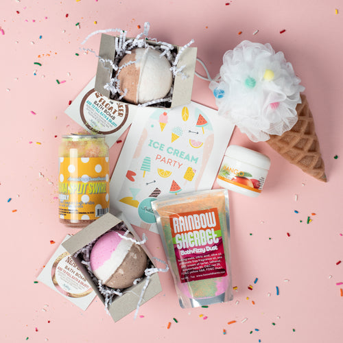 Collection of bath products and a bath bomb on a pink background with ice cream-themed packaging.
