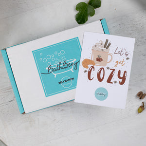 Open box with a 'BathBerry' label and a 'Let's get cozy' card on a light gray surface.