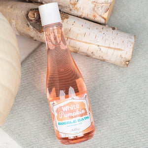 Bottle of White Pumpkin bubble bath on a textured surface with birch logs in the background
