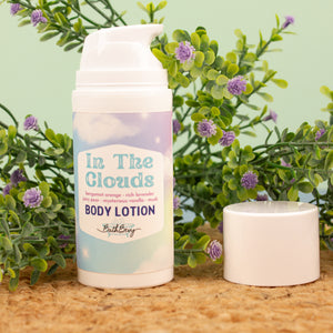 Body lotion bottle labeled 'In The Clouds' with a plant and candle in the background
