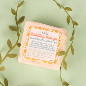 Two pink shower steamer cubes with labels on a light green background with leaf patterns.