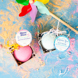 Two bath bombs in boxes with colorful labels on a textured blue background.