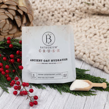 Load image into Gallery viewer, Bathorium Crush Ancient Oat Hydration package with a scoop of product and festive elements on a wooden surface.