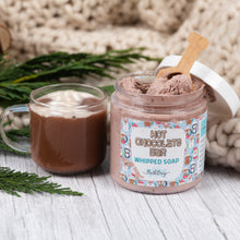 Load image into Gallery viewer, Jar of 'Hot Chocolate Bar Whipped Soap' with a spoonful of soap on a wooden surface next to a mug of hot chocolate.