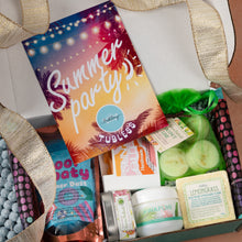 Load image into Gallery viewer, An open gift box filled with assorted self-care and beauty items, including a colorful 'Summer party' card, tealights in a green bag, a lemongrass soap bar, a small tin, and other packaged products, with a gold ribbon around the box.