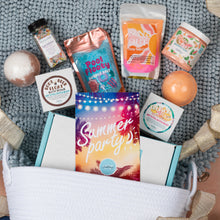 Load image into Gallery viewer, A curated summer bath and body gift set arranged in a white basket on a gray knit blanket. The set includes a 'Summer party!' card, a pouch of Pool Floaty Fizzy Salt, a Suns Out Fizzy Bath Dust, a Tropical Peach Bath Bomb, a body scrub, and other bath products.