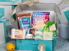 Load image into Gallery viewer, An open turquoise gift box filled with summer-themed pool and spa products, including a colorful 'Summer Party' card, a blue floatation bag, a green coconut lime set of tealights,, a lemon, and small toiletries, set on a light blue textured rug.