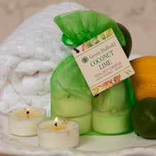 Load image into Gallery viewer, Green Daffodil Coconut Lime hand poured soy candles in a green mesh bag, displayed on a white tray with two lit tealight candles, a white towel, and citrus fruits.