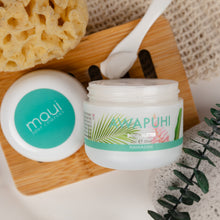 Load image into Gallery viewer, A jar of Maui Soap Company Awapuhi Hawaiian body butter with its lid beside it, styled on a wooden board with a sponge, spoon, and green leaves.