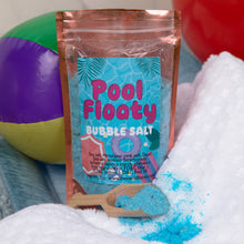 Load image into Gallery viewer, A stand-up pouch of 'Pool Floaty Bubble Salt' surrounded by white towels, a small wooden scoop filled with bright blue salt, and colorful beach balls in the background.