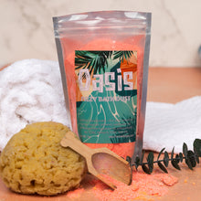 Load image into Gallery viewer, A stand-up pouch of Oasis Fizzy Bath Dust in a bright orange-pink color, styled with a yellow sponge, a wooden scoop, and a small eucalyptus sprig on a wooden surface with white towels in the background.