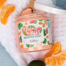 Load image into Gallery viewer, A jar of Bath Bevy Melon Mist Whipped Soap sits on a white towel, surrounded by orange slices and a small wooden scoop. The clear jar shows the pink whipped soap inside, with a colorful label featuring watermelon and citrus illustrations.