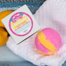 Load image into Gallery viewer, A pink and yellow half-and-half bath bomb sits on a white textured towel next to its white packaging box, which features a colorful pink and yellow label reading 'Raspberry Lemonade Bath Bomb'.