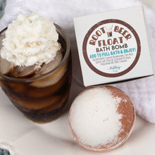 Load image into Gallery viewer, A bath bomb product scene showing a white box labeled 'ROOT BEER FLOAT BATH BOMB' next to a round bath bomb with white powder and brown rim, plus an iced coffee glass topped with whipped cream on a white towel background.