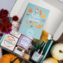 Load image into Gallery viewer, An open gift box styled with autumn decorations, featuring a light blue card that reads 'hello autumn' with fall illustrations. Inside the box are assorted gift items including a pumpkin spice bath bomb, lavender pajamas whipped soap scrub, a candle, and a bottle of bubble bath, surrounded by pumpkins and flowers.