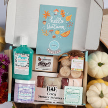 Load image into Gallery viewer, An autumn-themed gift box filled with curated self-care and bath products, including a turquoise body wash, lavender whipped soap, shower steamers, bath salts, and a blue 'hello autumn' card, surrounded by fall decorations like pumpkins and flowers.