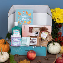 Load image into Gallery viewer, An autumn-themed bath gift box set from Bath Bevy, styled with seasonal props like pumpkins, an apple, and yellow flowers against a blue background.