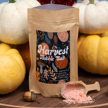 Load image into Gallery viewer, A kraft paper stand-up pouch labeled 'Harvest Bubble Salt' is displayed on a wooden surface with pink salt spilled in front and a small wooden scoop. White and yellow pumpkins surround the product, creating a seasonal autumn setting.