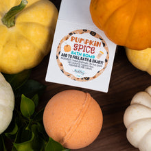Load image into Gallery viewer, A square white box labeled 'Pumpkin Spice Bath Bomb' sits on a dark wooden surface surrounded by decorative pumpkins and green leaves. An orange bath bomb is placed in front of the box.