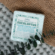 Load image into Gallery viewer, A square shower steamer cube package labeled 'Easy Breathe-y Eucalyptus Shower Steamer Cube' by Bath Body Works, placed on a textured gray knit surface with burlap and eucalyptus stems as props.