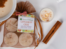 Load image into Gallery viewer, A packaged soy candle set labeled Green Daffodil Cinnamon Chai, shown with four round wax candles in a sheer brown bag, a lit white candle in a glass holder, cinnamon sticks, and a bowl on a white background.