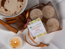 Load image into Gallery viewer, Four round soy candles in a sheer brown drawstring pouch with a printed tag reading 'Green Daffodil Cinnamon Chai,' styled on a white surface with cinnamon sticks, a bowl of cinnamon-spiced drink, and a lit tea light candle.