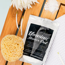 Load image into Gallery viewer, Unwind Steamers Dust packet with a sponge on a wooden surface with flowers.