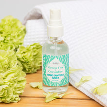 Load image into Gallery viewer, Hand sanitizer spray bottle labeled 'Green Tea + Cucumber' with green flowers and a white towel in the background.