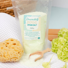Load image into Gallery viewer, Epsom salt packaging with a wooden spoon and bath accessories on a light background