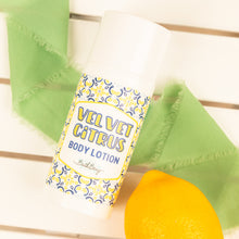 Load image into Gallery viewer, Body lotion bar labeled 'Velvet Citrus' with green towel and yellow sponge on a wooden surface