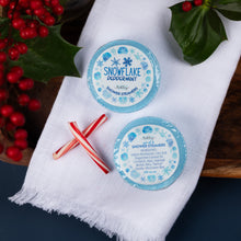Load image into Gallery viewer, Two snowflake-themed shower steamers on a white towel with holly leaves and berries in the background.