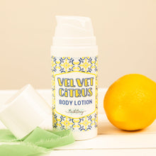 Load image into Gallery viewer, Body lotion bottle labeled 'Velvet Citrus' with a lemon and green towel on a beige background