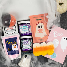 Load image into Gallery viewer, A Halloween-themed bath and body gift set arranged in a box with faux cobwebs, featuring a pink 'Boo' card, orange and bath bombs, a purple 'BOO' whipped soap jar, a pouch 'Spooky fizzy Dust' pouch, a Latika ghost bath soak packet, and a yellow-and-orange gradient bath bomb