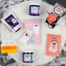 Load image into Gallery viewer, A styled flat-lay of a Halloween-themed bath and body gift set on a white marble surface with cobwebs. The set includes a pink 'Spooky' bath fizzy dust pouch, a purple 'Boo' whipped soap jar, a white ghost-shaped bath bomb, a pink 'Boo' card, a peach 'Latika' bath bomb packet, a purple whipped soap scrub jar, a white and orange bath bomb, and a black spiderweb decoration.