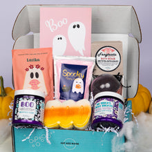 Load image into Gallery viewer, A curated Halloween gift box set from Bath Bevy featuring a pink 'Boo' insert card, a pink 'Latika' bath soak, a 'pooky Fizzy Dust' pouch, a 'Fangtastic' bath bomb, a purple 'No Tricks, Just Treats Whipped Soap Scrub jar, a yellow and orange striped BOO bath bomb, and a purple whipped soap jar, all arranged inside an open teal box with shredded paper filler and small pumpkins in the background.