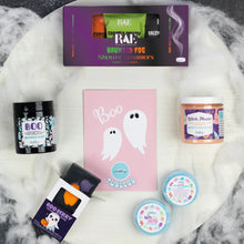 Load image into Gallery viewer, A Halloween-themed shower steam gift set arranged on a white marble surface with faux cobwebs. The set includes a purple RAE shower steam box, a pink Tubless card, a black Boo scented whipped soap jar, a Witch, Please whipped soap scrub, and two small colorful shower steamers.