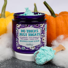 Load image into Gallery viewer, A jar of Bath Bevy whipped soap scrub with a purple label reading 'No Tricks Just Treats' and 'Whipped Soap Scrub,' shown open with bright aqua scrub on a wooden spoon, styled with pumpkins and white faux fur.