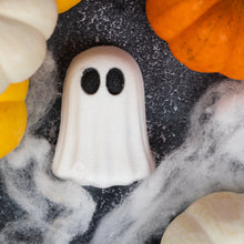 Load image into Gallery viewer, A white ghost-shaped Halloween bath bomb with black eyes, surrounded by orange and white pumpkins and white faux cobwebs on a dark textured surface.
