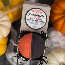 Load image into Gallery viewer, A split-color bath bomb in an open kraft paper box, surrounded by decorative pumpkins and white cobwebbing. The top label reads 'Fangtastic' and 'BATH BOMB'.
