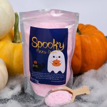 Load image into Gallery viewer, A stand-up pouch of Spooky Fizzy Dust bath salts in pink, styled with decorative pumpkins, white cobwebs, and a wooden scoop of the pink salt in the foreground.