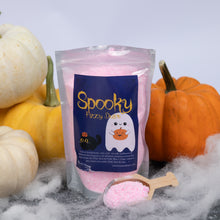 Load image into Gallery viewer, A stand-up pouch of pink bath salts labeled 'Spooky Fizzy Dust' is centered on a gray surface with decorative pumpkins and white cobwebbing around it. A small wooden scoop filled with pink bath salts sits in front of the pouch.