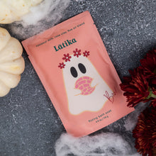 Load image into Gallery viewer, A pink pouch of Latika fizzing Bath Soak is styled in a flat lay on a textured gray surface, surrounded by white pumpkins, white faux cobwebbing, and dark red chrysanthemums.
