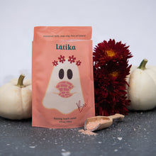 Load image into Gallery viewer, A peach-colored stand-up pouch of LĀtika fizzing bath soak stands on a dark textured surface, styled with white pumpkins, dark red flowers, and a small wooden scoop of pink bath salts in front.
