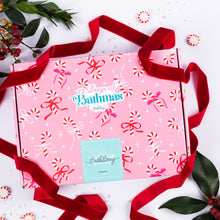 Load image into Gallery viewer, A pink 12 Days of Bathmas advent box with a red velvet ribbon, decorated with candy canes and bows, on a white background with holiday greenery. Bath bomb advent calendar
