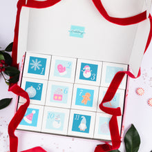 Load image into Gallery viewer, An open white 12 Days of Bathmas Advent calendar box with 12 numbered square compartments decorated with winter and holiday illustrations, tied with a red ribbon, photographed on a light pink surface with holiday greenery and candy props.